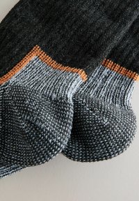 Strikkede sokker i mørkegrå med lysegrå accenter og orange detaljer. Har ribbet manchet og struktureret syning. Rund tå konstruktion.
