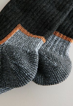 Sötét szürke kötött zoknik világosszürke díszítéssel és narancssárga részletekkel. Bordás passzé és texturált varrás jellemzi. Kerek orrú kivitel.