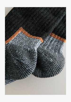 Neuleet sukat tummanharmaana, vaaleanharmailla yksityiskohdilla ja oranssilla korostuksella. Tekee resorikannan ja teksturoidun ompelun. Pyöreä varvasrakennus.