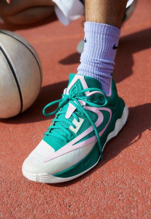 Chaussure de sport turquoise et blanche avec des accents roses, dessus en maille texturée et semelle en caoutchouc incurvée, associée à des chaussettes côtelées lavande.