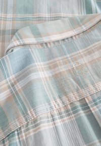 Camicia a quadri blu chiaro e beige realizzata in un tessuto morbido, con colletto button-down e un piccolo logo ricamato sul petto.