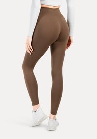 Bruine hoge taille leggings gemaakt van rekbaar materiaal, met een gladde textuur en een nauwsluitend ontwerp. Gemaakt met witte sneakers.