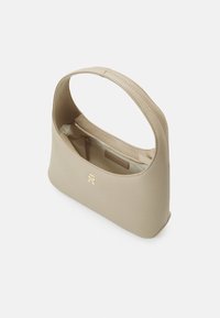 Beige skuldertaske lavet af glat materiale med et buet håndtag og en lomme med lynlås indvendigt. Guld hardware logo detalje på forsiden.