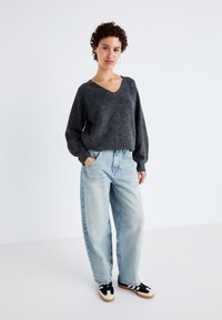 Maglione grigio a maglia con scollatura a V, abbinato a jeans baggy in denim chiaro. Le scarpe presentano un design a strisce in bianco e nero. Design semplice e vestibilità rilassata.
