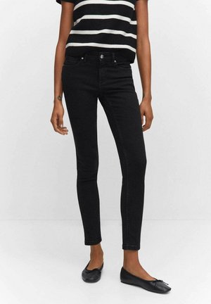 Person wearing black skinny jeans, black and white striped short-sleeve top, and black ballet flats, standing against a plain background.