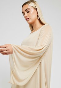 Beige blus med flödande, långa ärmar i en mjuk och lätt textur samt rundad halsringning. Subtil drapering ger en extra designdetalj.