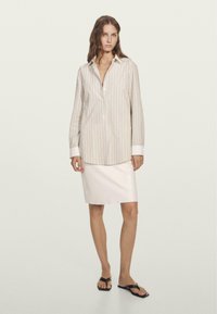 Striped button-up shirt with long sleeves and white cuffs paired with a fitted, light-colored skirt and black flip-flops.