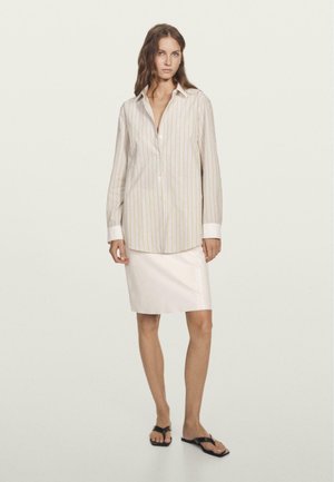 Camicia a righe con maniche lunghe e polsini bianchi abbinata a una gonna aderente di colore chiaro e infradito nere.