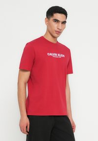 Κόκκινη βαμβακερή μπλούζα με στρογγυλή λαιμόκοψη. Διαθέτει λευκό λογότυπο "CALVIN KLEIN" και κείμενο "ESTABLISHED 1968" μπροστά. Κοντομάνικη.