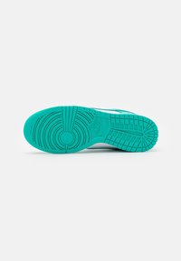 Semelle d'une basket turquoise avec des motifs de bande de roulement circulaires et rectangulaires et un logo Nike visible au centre.