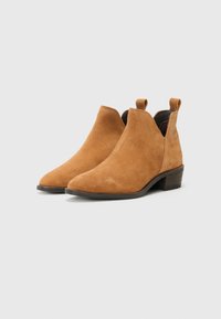Bottines en daim tan avec un bout pointu, un petit talon en bloc et des languettes sur les côtés. Texture lisse et design simple.