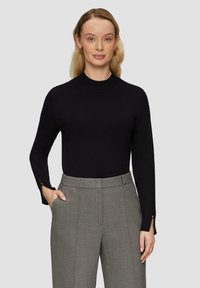 Zwarte langwaardige top met een hoge halslijn en subtiele manchetten, gecombineerd met grijze op maat gemaakte broek met zakken en een soepele textuur.