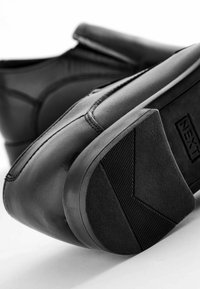 Schwarze Lederschuhe mit sleekem Design, ausgestattet mit einer strukturierten Gummisohle und elastischen Seitenpaneelen für einfaches An- und Ausziehen.