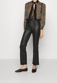 Blusa transparente de estampado de leopardo con cuello de lazo, combinada con pantalones de cuero negros de talle alto y bailarinas negras.
