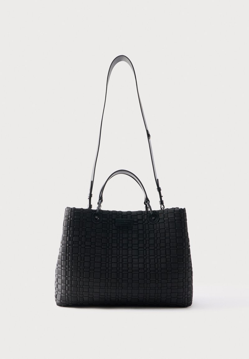 Μαύρη υφασμένη δερμάτινη τσάντα χειρός με δύο κοντές λαβές και έναν μακρύ ρυθμιζόμενο ιμάντα ώμου, παρουσιάζεται πάνω σε μονόχρωμο φωτεινό φόντο.