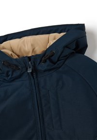Marinejacke mit beigem Innenfutter, ausgestattet mit Kapuze, Frontreißverschluss, Kordelzugverstellungen und einer flachen Tasche auf einer Seite.