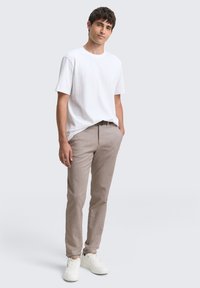 Witte katoenen t-shirt gecombineerd met beige slim-fit broek. Model draagt witte sneakers. Eenvoudig ontwerp, ontspannen pasvorm en minimalistische stijl.
