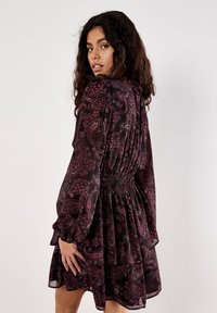 Robe noire à manches courtes avec un motif paisley en rouge foncé et blanc, taille cintrée, jupe fluide et manchons à volants.