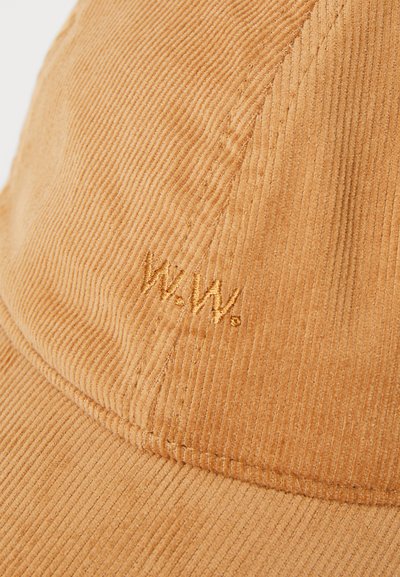 Siltā oranžā corduroy cepure ar tekstūrētām rievām. Priekšējā panelī ir izšūts "W.W." logo, kas atbilst krāsai.