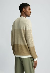 Sweter dziany w odcieniach brązu i kremu z teksturowanym wzorem, wyposażony w ściągacze przy mankietach i u dołu. Luźny krój, okrągły dekolt i długie rękawy.