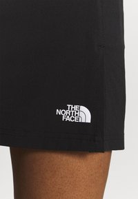Pantalones cortos negros de tejido ligero con el logo blanco de "The North Face" en el dobladillo inferior izquierdo. Textura suave y diseño sencillo.