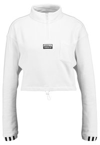 Vit croppad sweatshirt med hög krage, framdragkedja, liten bröstficka och svart adidas-logga. Har randiga ärmslut och dragsko i nederkant.