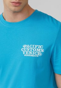 Blauwe katoenen t-shirt met ronde hals, voorzien van een witte grafische print met de tekst "PACIFIC CUSTOMS VENICE BOARDS&KITS." Soepele textuur.