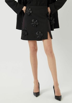 Sort mini nederdel med strukturerede blomsterapplikationer, sideslidsdetalje og glat stof. Sammen med elegante spidse hæle.