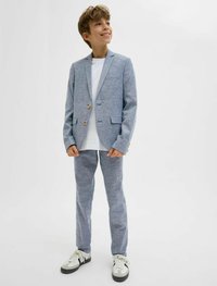 Világoskék öltöny, texturált felülettel, egysoros zakóval, két gombbal és hozzá illő nadrággal. Fehér pólóval és sportcipővel párosítva.