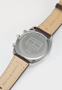 Montre en acier inoxydable argenté avec un fond gravé du logo, bracelet en cuir véritable marron clair, matériel en acier inoxydable et détails résistant à l'eau.