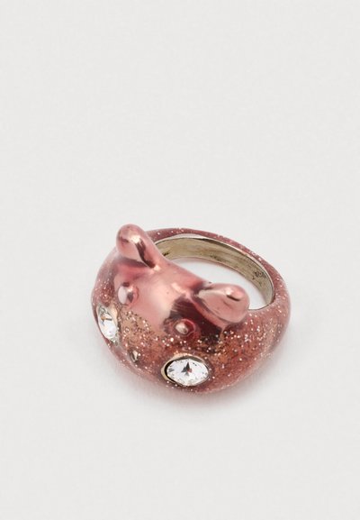 Bague à paillettes roses avec un dessus en forme d'ours, agrémentée de deux accents en gemmes transparentes. Texture lisse avec des bords arrondis.