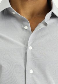 Lichtgrijs, gestreept shirt met een button-down kraag, witte knopen en een gladde stoftextuur. De nek is zichtbaar.