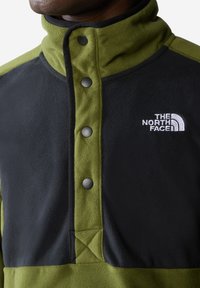 Polarowy sweter w oliwkowym zielonym i czarnym kolorze z wysokim kołnierzem, napami i haftowanym logo na piersi. Miękka tekstura, kontrastujące kolory.