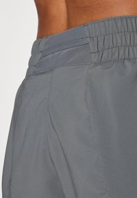 Los pantalones cortos deportivos grises cuentan con una cintura elástica texturizada con un inserto de malla, costuras evidentes y una tela lisa y ligera.