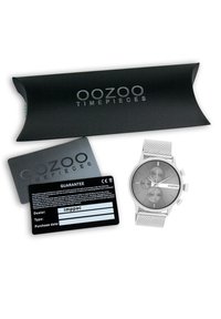 Montre avec bracelet en maille argentée, plusieurs cadrans, face grise et carte de garantie noire dans un tube d'emballage noir, de la marque "oozoo timepieces."
