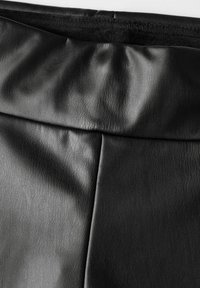 Zwart faux leren materiaal met een gladde textuur en subtiele nerven. Heeft geplooide details bij de tailleband voor extra ontwerpintrige.