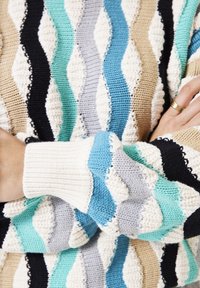 Gebreide trui met een golvend patroon in beige, zwart, lichtblauw, teal en grijs. Voorzien van ribbenmanchetten en een gestructureerde afwerking.
