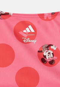 Rózsaszín szövet piros pöttyökkel, amelyen Disney logó és Mickey Mouse grafika található. Simább textúra, kontrasztos fehér részletekkel.