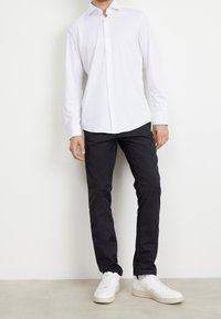 Witte overhemd met knoopsluiting, lange mouwen, gecombineerd met donkere broek en witte sneakers. Eenvoudig ontwerp, slanke pasvorm, gladde textuur.