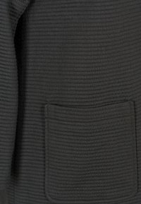 Czarna tkanina o fakturze z prążkowanym wzorem, wyposażona w przednią kieszeń naszywaną. Miękki, ciepły materiał odpowiedni na odzież wierzchnią.