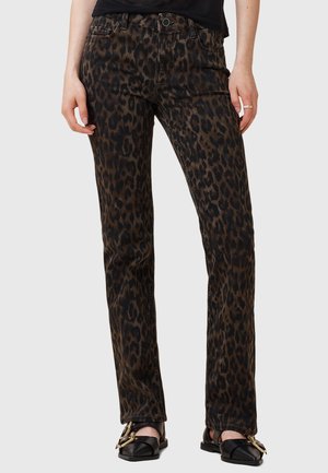Frau trägt schwarze und braune Leo-Print-Jeans mit geradem Bein und schwarze spitze Ballerinas mit goldenen Schnallen. Hände entspannt an den Seiten.