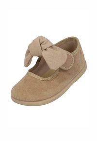 Zapato de tela beige con una punta suave y redondeada, cinta elástica y un gran lazo en la parte frontal. Suela plana con un acabado texturizado.