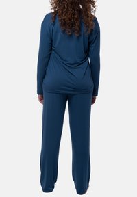 Tummansininen, pitkähihainen toppi rennolla leikkauksella, yhdistettynä samaan sävyyn löysiin housuihin, jotka on valmistettu pehmeästä ja kevyestä kankaasta.