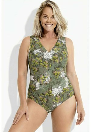 Uśmiechnięta kobieta w zielonym, białym i żółtym jednoczęściowym kostiumie kąpielowym z wzorem, na jednolitym białym tle.