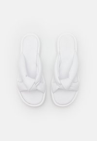Vita skidsandaler med en knuten remdesign, släta syntetiska material, vadderad innersula och en platt gummisula.