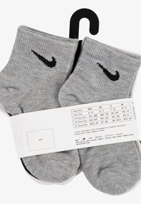Szare skarpetki do kostek z czarnym logo Nike w kształcie ptaka (swoosh). Materiał prążkowany o wyraźnej teksturze. Dołączona metka zawiera informacje o rozmiarze i wskazówki dotyczące pielęgnacji.