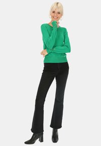 Zielony sweter z dzianiny z długimi rękawami i złotymi detalami w postaci guzików, zestawiony z czarnymi dżinsami w kształcie dzwonów oraz czarnymi botkami na obcasie.