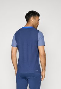 Marineblå kortærmet atletisk skjorte med tekstureret stof, blå detaljer ved kraven og subtile lodrette mønstre. Tætsiddende design til aktiv sport.