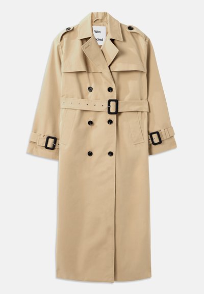 Μπεζ παλτό trench κατασκευασμένο από ανθεκτικό ύφασμα, με διπλό κούμπωμα, φαρδιές πέτες, ζώνη στη μέση και αξεσουάρ με κρίκους στα μανίκια.
