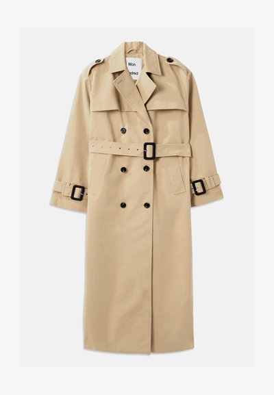 Μπεζ παλτό trench κατασκευασμένο από ανθεκτικό ύφασμα, με διπλό κούμπωμα, φαρδιές πέτες, ζώνη στη μέση και αξεσουάρ με κρίκους στα μανίκια.